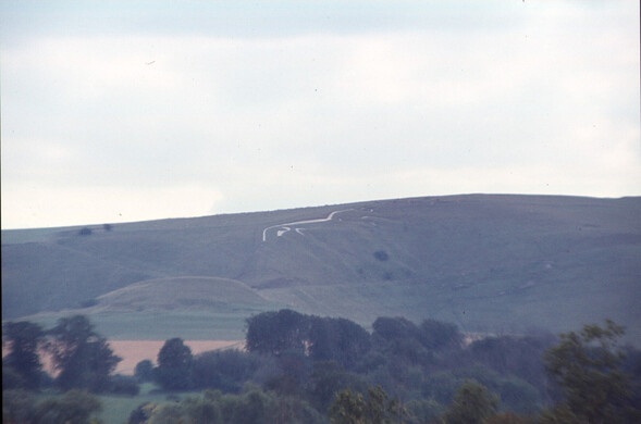 An outline of a white horse shape carved into a hill in the distance.