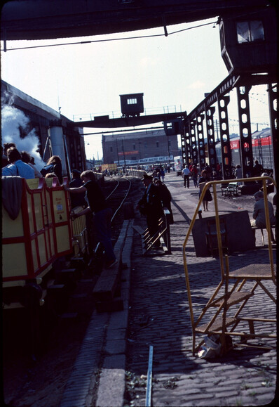 A steam engine pulls wagons with families in, under a surrounding metal gantry.