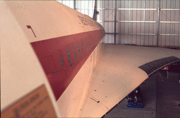 Looking down the body of the outside of the Concorde;  There's a red stripe along the, white, body, over the windows; the wing has numbers marked on in sequence near the middle of the edge.