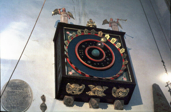 An old clock, whose dial shows an earth at the centre with a moon and sun orbiting around it.  It also has a numerical dial.  It's decorated with angels etc.