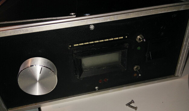 The front of a home built FM radio receiver; it is black with a big shiny tuning knob, an LCD frequency display, with 2 tuner LEDs below it and a bargraph display above; there's a big power switch and two unlabelled small toggles with corresponding LEDs.