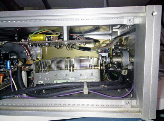 Looking into the side of the radio, we see an aluminium frame with no idea what to unscrew next.  There's a chunky variable capacitor,  a torroidal transformer at the back with various boards and components interconnected.