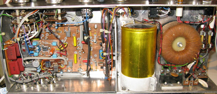 The underside of my dad's hifi amp; a big fat capacitor sits next to a torroidal transformer; wires run from siwtches and potentiometers on the front panel to the hand soldered board and sockets on the back.