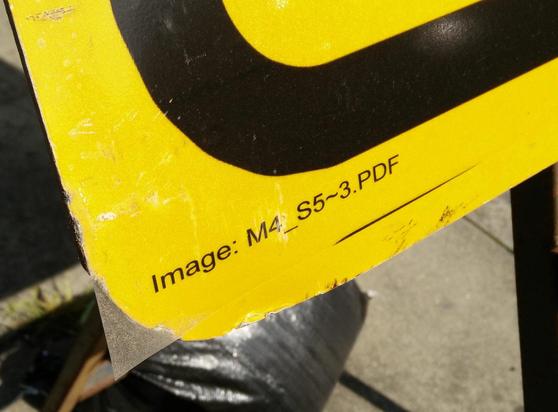 The corner of a temporary road sign, on a pavement - where it's got the PDF name; it's printed on a transparent sheet stuck to the yellow metal.