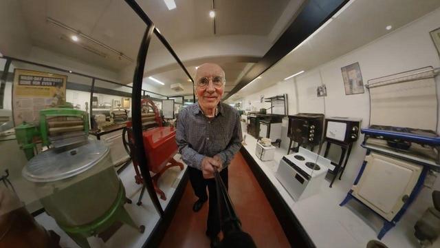 a frame from the video showing Tim Hunkin walking around an exhibit of household items at the science museum.