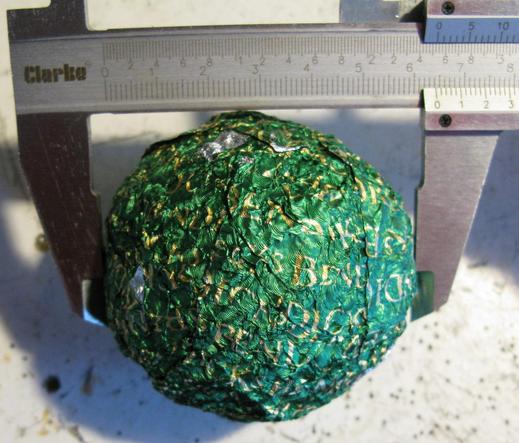 A vaguely spherical ball of green foil wrappers, from Bendicks mints (the name is printed on them in a beige/yellow) being measured in a pair of callipers.