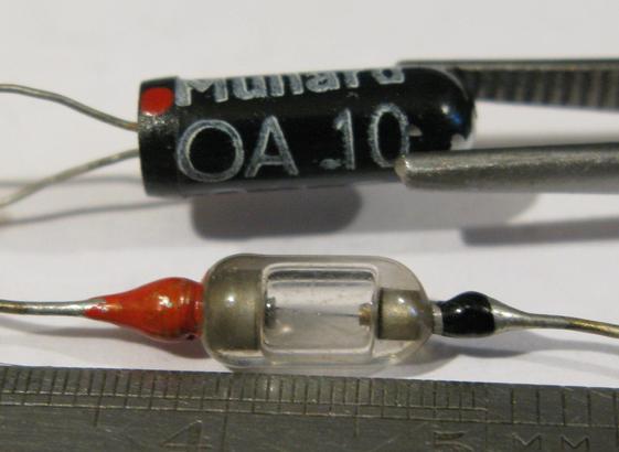 Two old diodes sit next to a ruler; one is held in tweezers. They're both about 1cm long.
The top one a Mullard OA10 and is a black rounded cylinder with two wires at one end.  It has a small red dot.
The bottom is a real lovely one; a tiny glass envelope, silvered on the ends, shows a tiny wire - presumably contacting a chunk of germanium.  One wire is at each end, one is painted red, the other black.