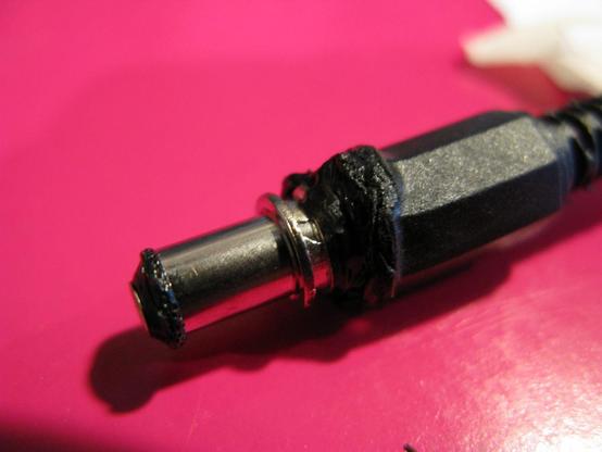 A barrel jack PSU plug, gently melted around the collar and the end.
On a tasteful light pinky-purple background.