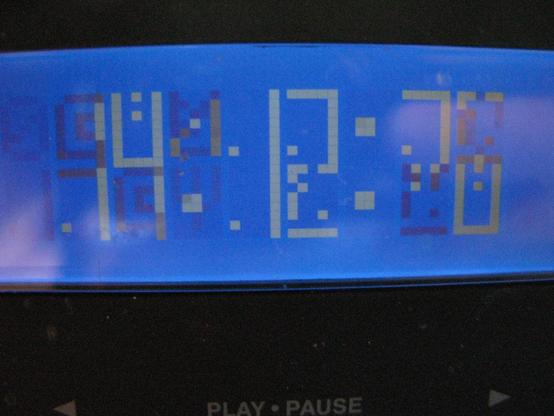 A very corrupt LCD display of a clock; that is trying to read 14:12:26 - there are random pixels splatted all over; there are places where random other characters have been displayed.