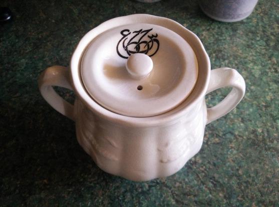 A small white pottery pot with two handles.  The lid has a steam hole and some Arabic writing.