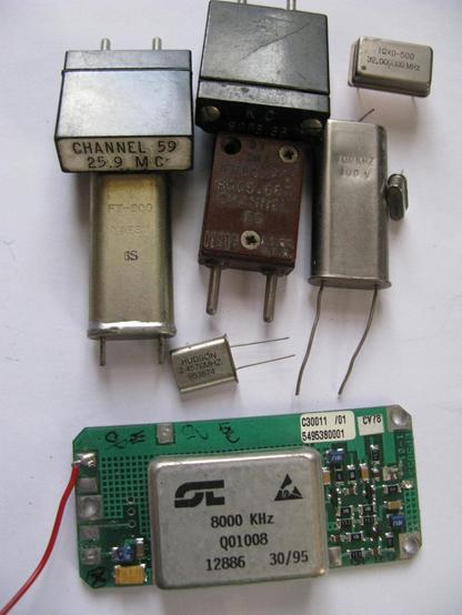 A collection of different quarts crystals in varying odd packages; some are very old (big old black modules, one of which is labeleld CHANNEL 59, 25.9 MC), modern 4 pin oscillator, an ancient  brown/red one labelled 8006(?).667 CHANNEL 63, two very tall but modern silver canned crystals, one marked FT-200, another marked 100KHz, a couple of small modern cans, and at the bottom a big module which is marked 8000KHz Q01008 which I assume is an ovened module.