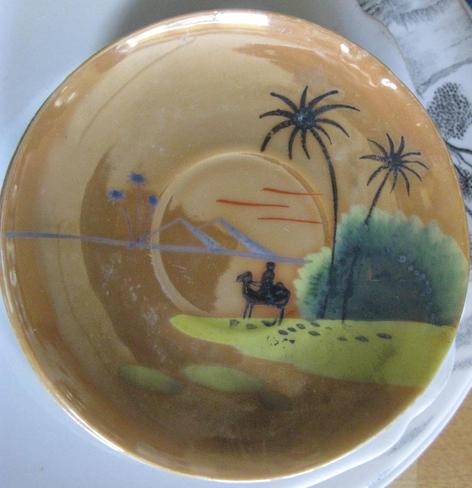 A saucer, with an imagined desert scene; it's a general shiny light brown, with a person riding a camel across some lighter sand, some palm trees, and a couple of bonus pyramids.  And hmm, a green bush??