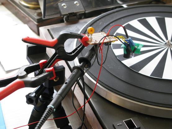 A turntable with a black/white striped paper disc on, over which is hanging a hacky optosensor wired to strip board held in place with a heath-robinson combination of clamps and camera tripod.  A scope probe is attached.