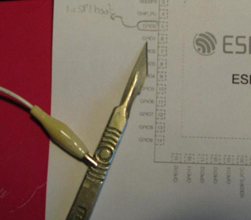 A sharp scalpel with a croc-clip lead attached.  It's sitting on a print out of the ESP32-S3 pinout.