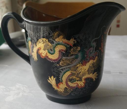 A black jug painted with very detailed dragons in gold red and green. The inside of the jug is a golden/brown colour. 
