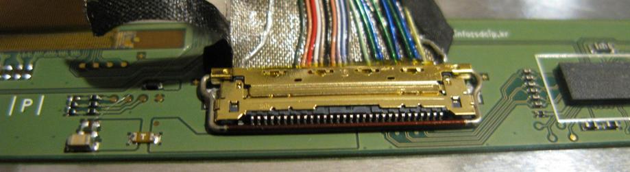 A close up of the connector on the back of an LCD panel; it's a 30 way connector with a nice brassish shell, and about 20 or so are connected.  There's conductive tape around the cable and it's on a PCB with a chip and various passives.