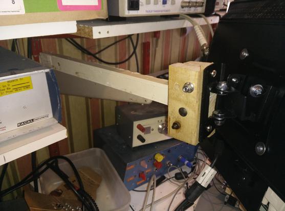 A tilt swivel monitor mount is screwed/bolted/bodged to bits of wood that are fixed to a metal shelf support..  In the background are random bits of old electronics lab equipment.