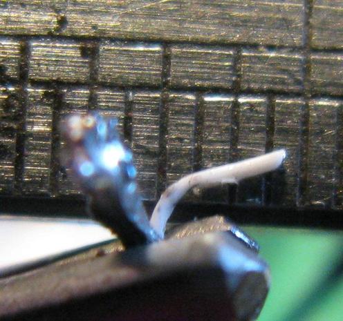 A tiny piece of coax shows an outer sheath that's been tinned and an in inner white section; it's against a ruler showing the inner is much under 0.5mm.
It's being held in what appears to be comically large tweezers.
