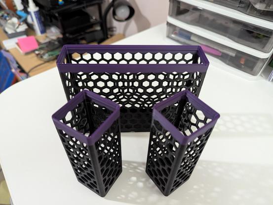 Some black desk organizer containers with a hexagonal side pattern accented with a purple top.
