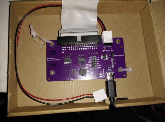 A greaseweazel USB->Floppy board, wired to a floppy cable and a USB-C; but mounted in a cardboard box.