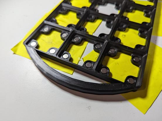 Close up of a grid of gridfinity bays with magnets with a handle at one end.