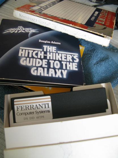 On a blueish towel lies the CD box sets of Phase 1 and 2 of the BBC Radio series of the HHGttG, behind it is a reel-to-reel tape box with HHGttG hand written on it; it has the radio series recorded from it's original broadcast.  In front is a box of Ferranti Computer Systems 5.25" disks.