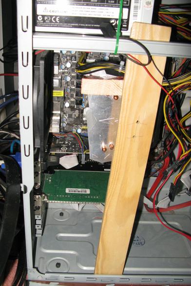 A PC case; with a chunk of wood and a wedge of wood pressing down on the CPU heatsink.
