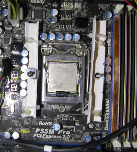 A PC motherboard showing the CPU, with a couple of bodged plastic mounts at the sides for where the fan should bolt to