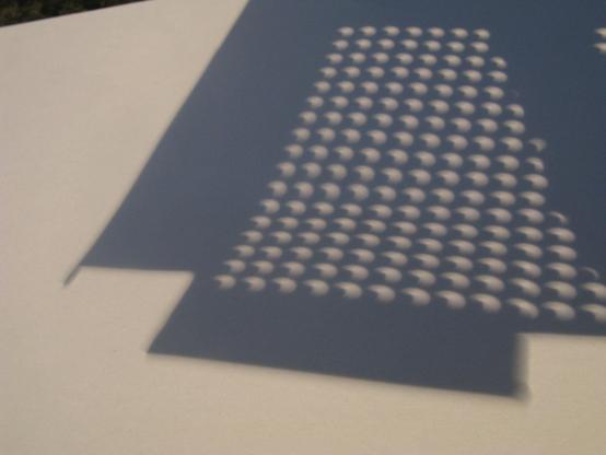 A few hundred arced projections of the sun seen through a perforated sheet onto a piece of white paper