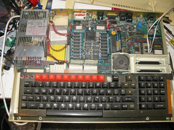 The top off the BBC Master 512 - in addition to the dust, we have the Master PSU, the CMOS battery pack, the Master 512 copro in the middle, fly leads going off to the switches, the speaker and cartridge slots, and some EPROMs.
